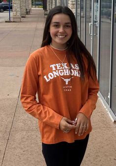 a girl standing in front of a store wearing an orange texas longhorn shirt and black leggings