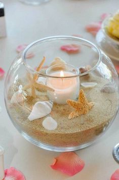 a glass bowl filled with sand and seashells on top of a white table