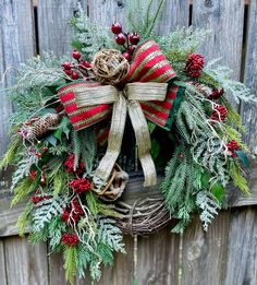 a wreath hanging on the side of a wooden fence with evergreens, berries and pine cones