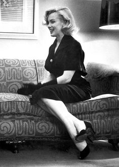 a black and white photo of a woman sitting on a couch with her legs crossed