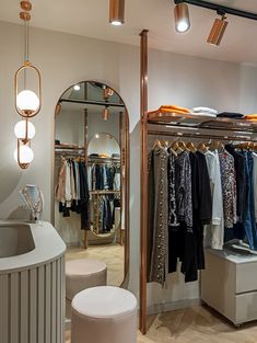 a clothing store with clothes on racks and stools in front of the mirror,