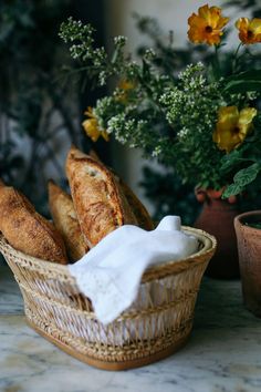 some bread in a basket on a table next to flowers and a potted plant