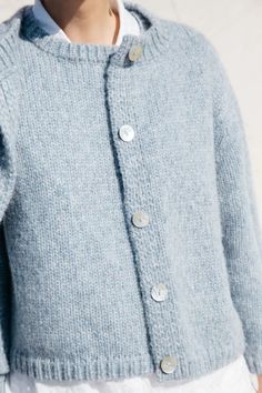 a close up of a person wearing a blue sweater and white pants with buttons on it