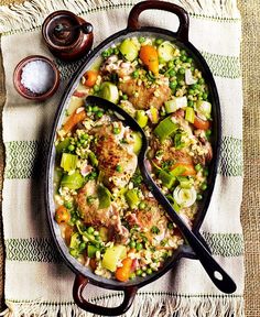 a skillet filled with rice and vegetables on top of a table next to two spoons