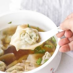 a person is holding a spoon over a bowl of dumplings and broccoli soup