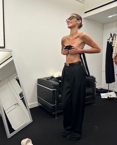 a woman standing in front of a mirror looking at her cell phone while wearing black pants