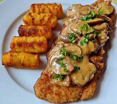 a white plate topped with meat covered in gravy next to fried potatoes and tater tots