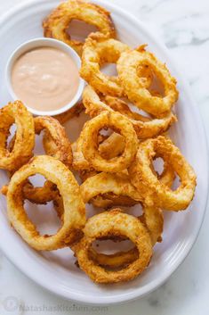 onion rings on a plate with dipping sauce in the middle, ready to be eaten