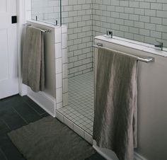 a bathroom with white tiles and black flooring, two towels hanging on the shower door