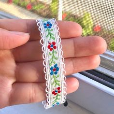 a hand holding a piece of white lace with red, blue and green flowers on it