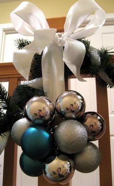 a christmas wreath with ornaments hanging from it's side and white ribbon on the front door