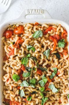 pasta with tomatoes and basil in a white casserole dish on a white surface