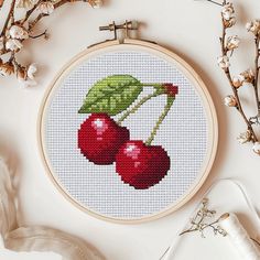 a cross - stitch pattern with cherries and leaves on it, next to some scissors