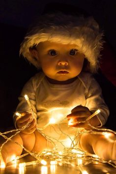 a baby wearing a santa hat sitting on top of a table covered in christmas lights