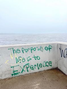 a wall with graffiti written on it next to the ocean in front of an overcast sky