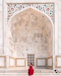 a woman in a red dress is standing on the steps of a marble building with an archway