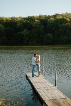 a man and woman kissing on a dock in the middle of a body of water