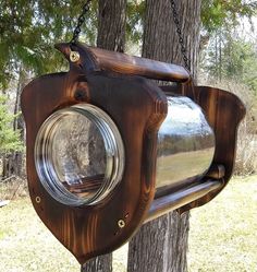 a bird feeder hanging from the side of a tree in front of some trees and grass