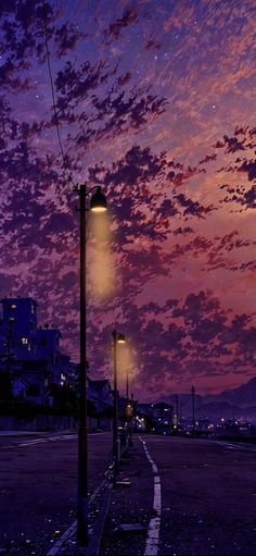 a street light sitting on the side of a road under a purple sky with clouds