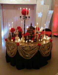 a table topped with lots of candles and red flowers next to a wall covered in curtains