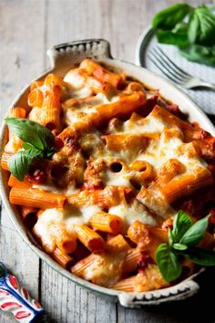 a pasta dish with meat, cheese and spinach on a wooden table next to utensils