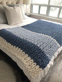 a bed with a blue and white blanket on top of it next to a window