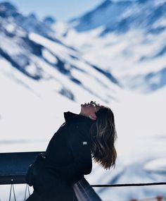 a woman standing on top of a snow covered mountain next to a ski lift with her eyes closed