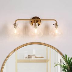 a bathroom vanity light with three lights and a round mirror over the sink in front of it