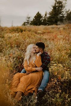 a couple cuddles in the tall grass during their fall engagement session at sunset