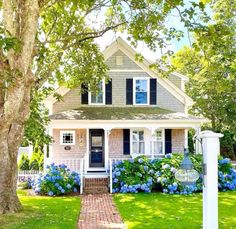 a house with blue flowers in front of it and a white picket fence around the yard