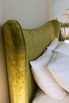 a green velvet headboard with white pillows on it and a painting in the background