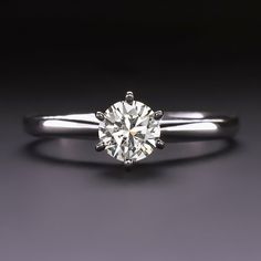 a white gold ring with a round diamond in the center on a dark background,