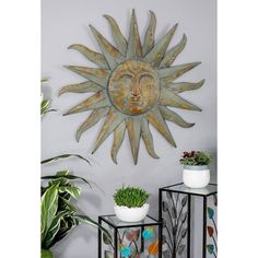 a metal sun wall hanging on the wall next to two planters and a potted plant