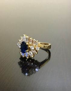 DeKara Designs Clearance Metal- 14K Yellow Gold, .583. Stones- 1 Oval Blue Sapphire 0.60 Carats, 4 Round Diamonds, 8 Square Baguette Diamonds, 6 Marquise Diamonds, G-H Color VS2-SI1 Clarity 1.10 Carats. Size- 6 1/4. FREE SIZING Handmade 14K Yellow Gold Sapphire and Diamond Ring. This ring is inspired by the Art Deco era with an enticing round fiery oval blue sapphire. The sapphire is set in between 4 prongs. The sapphire has a total of 18 round, baguette, and marquise diamonds on the top and the Gold Sapphire Cluster Ring With Brilliant Cut, Blue Cluster Ring For Formal Occasions, Formal Blue Cluster Ring, Blue Diamond Ring With 17 Jewels For Anniversary, Wedding Sapphire Ring With 17 Jewels In 14k Gold, Sapphire Diamond Ring With 17 Jewels For Wedding, Gold Cluster Ring With Sapphire Center Stone, Gold Cluster Sapphire Ring With Center Stone, Hallmarked Cluster Sapphire Ring For Wedding