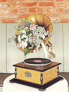 an old record player with flowers in it on top of a white table cloth covered pedestal