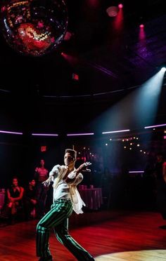 a man is dancing on the dance floor in front of a disco ball while people watch