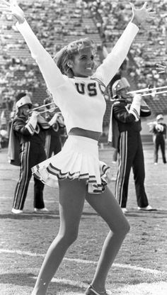 a cheerleader is dancing on the field with her arms in the air while other cheerleaders watch