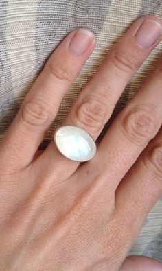 An elegant crystal white large oval Rainbow Moonstone has been set in sterling silver. The ring band is handmade from a fancy patterned sterling silver thick wire. This moonstone is pearly white and shines on its own with hues of pink, blue, and even orange. The luminescent quality of the moonstone makes this ring beautifully unique and elegant. The stone is 13mm x 18mm in size with a height of about 8mm. This moonstone can be set vertically (North to South) rather than horizontally as shown. Ju Modern Oval Cabochon Moonstone Ring, Modern Oval Moonstone Ring With Large Stone, Modern Oval Sterling Silver Moonstone Ring, Modern Adjustable Oval Moonstone Ring, Oval White Gold Moonstone Ring, Elegant White Moonstone Ring, Oval Cabochon, Elegant White Oval Cabochon Moonstone Ring, Minimalist Handmade White Moonstone Ring, Elegant White Moonstone Ring With Oval Cabochon