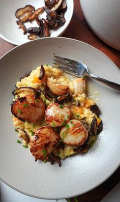 a white plate topped with scallops and mushrooms next to a bowl of mushrooms