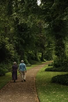 an older couple walking down a path in the park together, holding hands and looking at each other