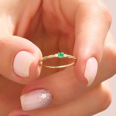 a woman's hand holding a gold ring with a green stone on the middle