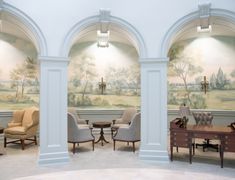 a room with chairs, tables and paintings on the wall behind two archways that lead to another room