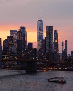 the city skyline is lit up at night as a boat passes under it on the water