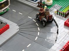 a lego model of a man driving a toy car on a street with buildings in the background