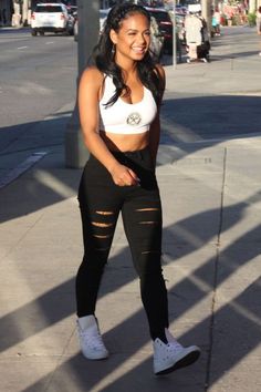 a woman is walking down the street in ripped black pants and white tank top with her hand on her hip