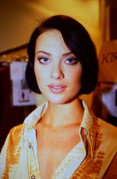 a woman with dark hair and blue eyes is posing for a photo in a yellow shirt