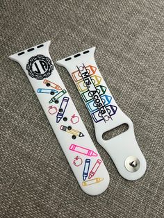 two white apple watch bands with school supplies painted on them, sitting on a gray surface