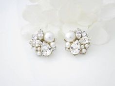 two pairs of earrings with pearls and crystals on them next to a white flower in the foreground