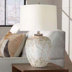 a white vase sitting on top of a wooden table next to a lamp and pillows