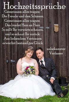 a man and woman sitting next to each other in front of a wooden fence with words written on it